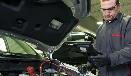 Nissan technician testing a battery under the hood with a diagnostic tablet